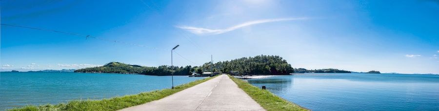 Une route dégagée qui mène à un lac, avec une petite île en son centre.