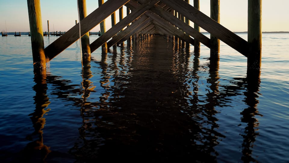 A wooden pier extending into calm water with a clear sky in the background.