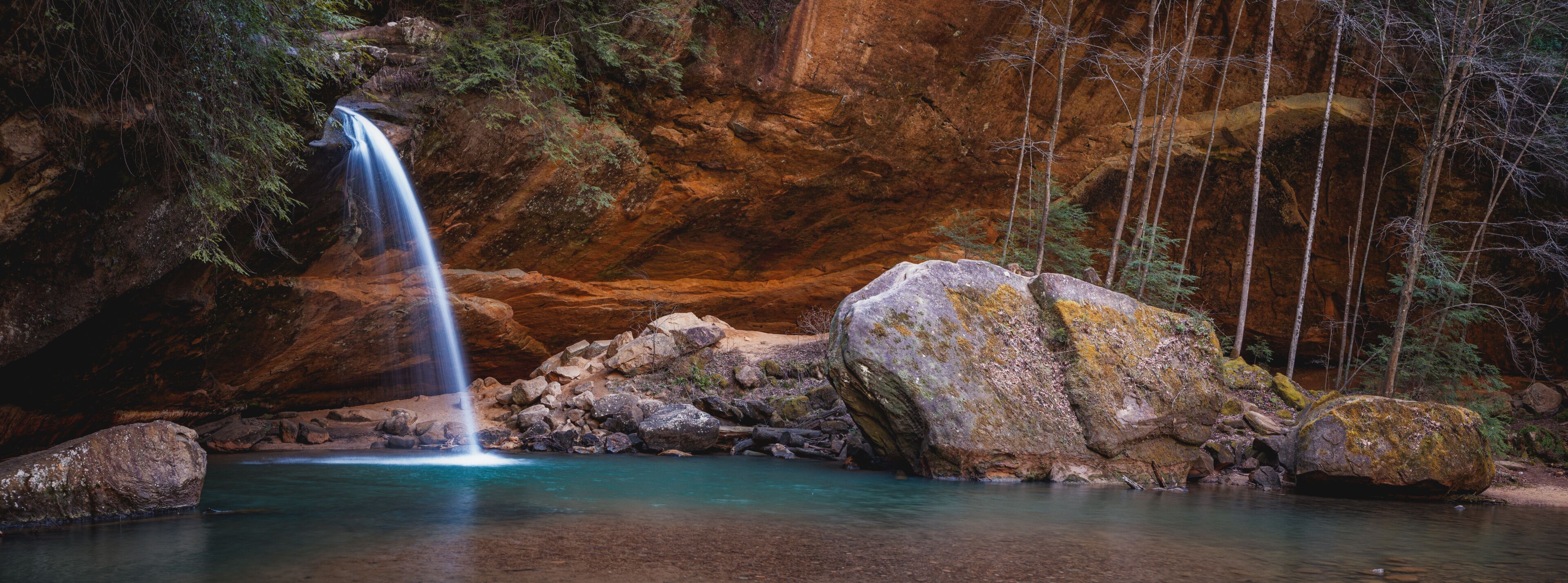 A waterfall, clear water, rocky terrain, and forested area.