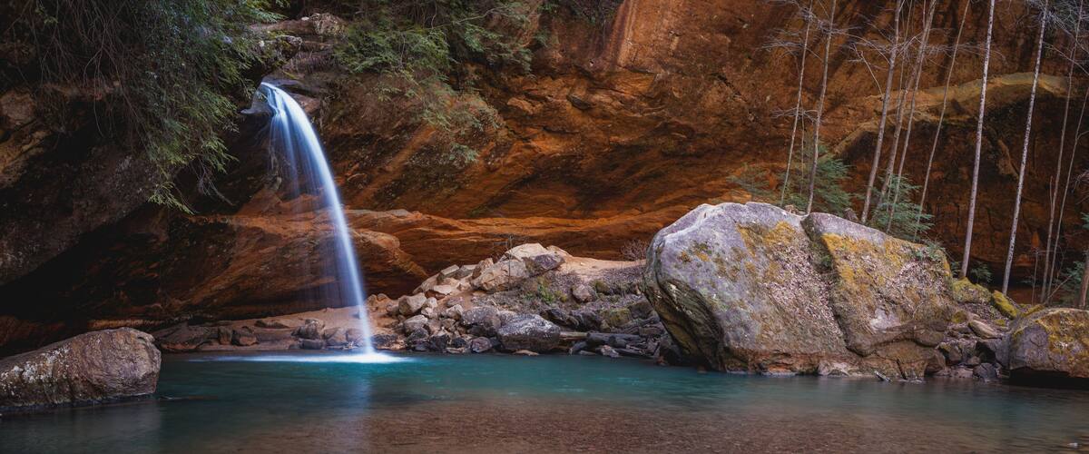 A waterfall, clear water, rocky terrain, and forested area.