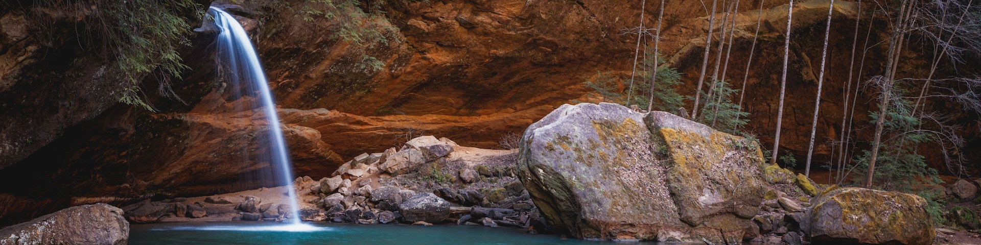 A waterfall, clear water, rocky terrain, and forested area.