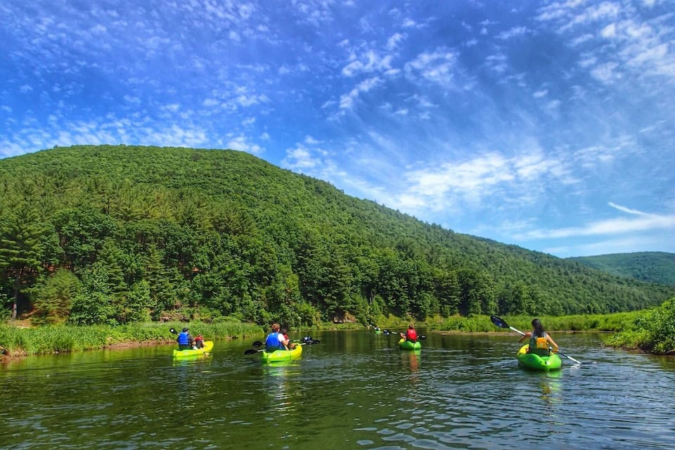 People kayaking on a river surrounded by lush green hills.
