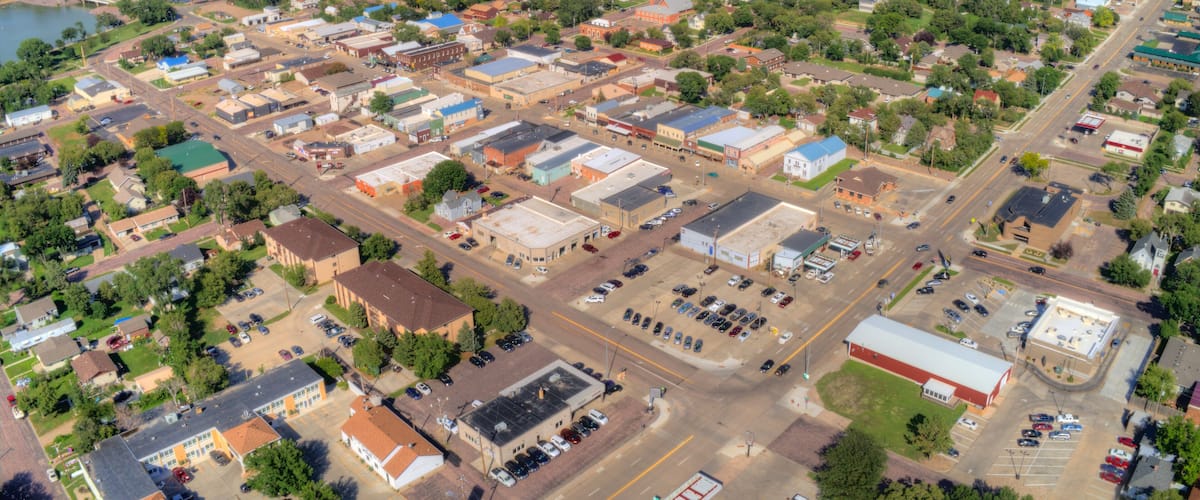 An aerial view of a town with a river, green hills, and a mix of residential and commercial buildings.
