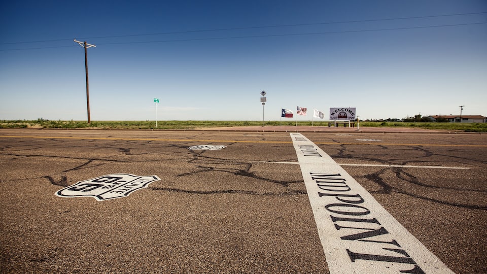 A road with 'Midpoint' marking, a 'Welcome' sign, and a 'Route 66' symbol.