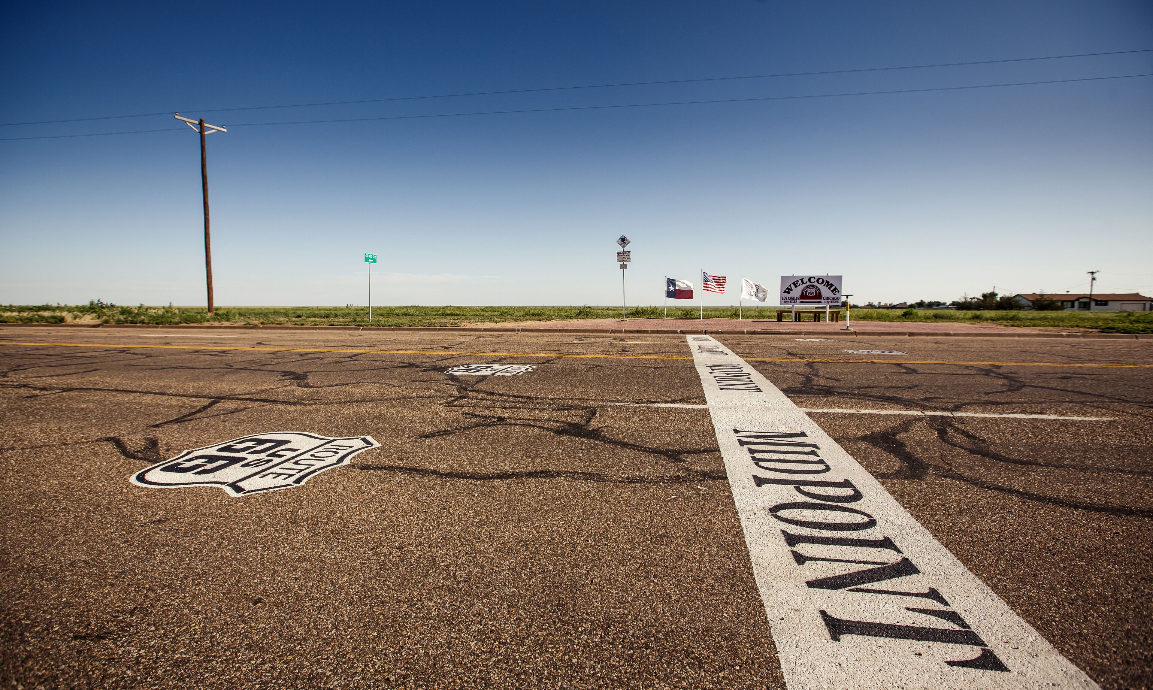 A road with 'Midpoint' marking, a 'Welcome' sign, and a 'Route 66' symbol.