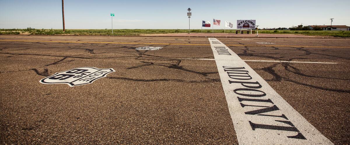 A road with 'Midpoint' marking, a 'Welcome' sign, and a 'Route 66' symbol.