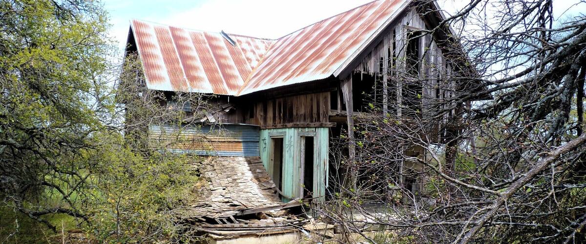 An abandoned building with a rusted metal roof and overgrown vegetation.