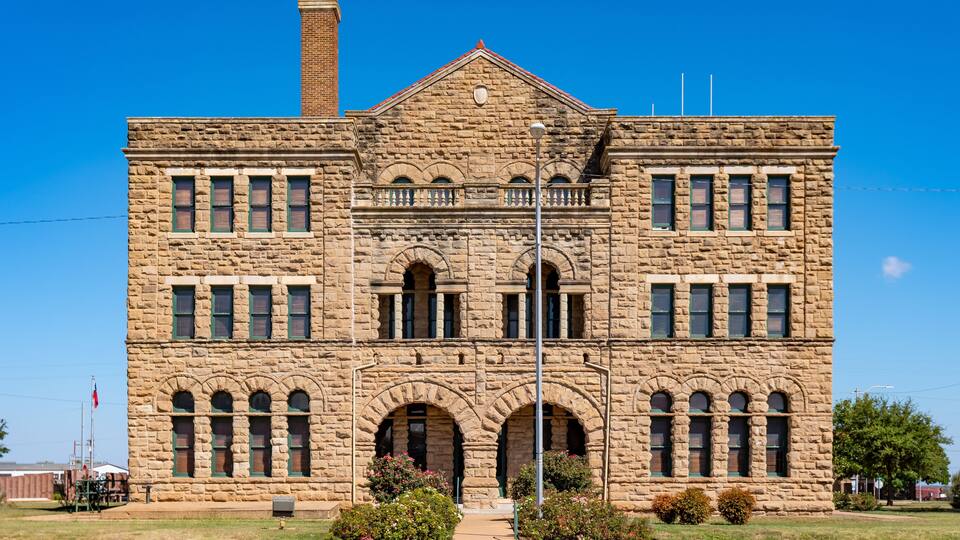 A large stone building with a prominent chimney, arched windows, and a balcony.