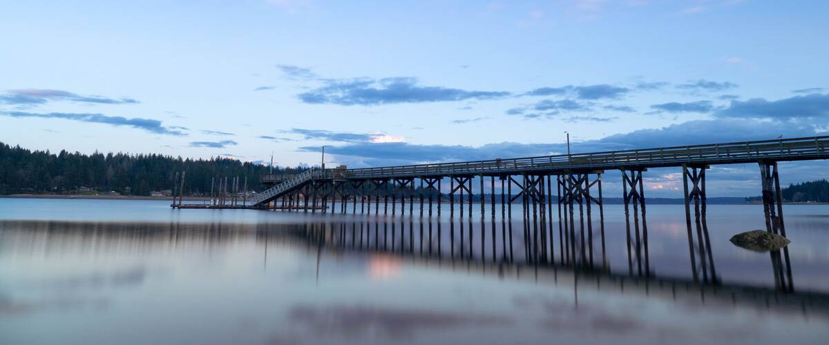 A long pier extending into a calm lake with a clear sky above.