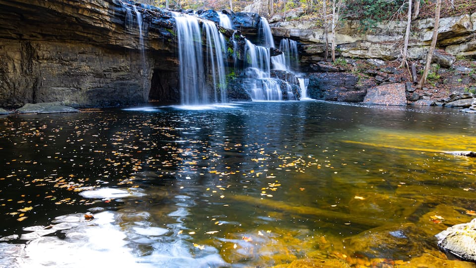 A waterfall cascading into a clear pool surrounded by autumn foliage.