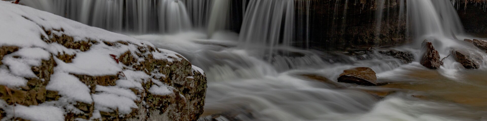 Una cascada cubierta de nieve con rocas y árboles al fondo.