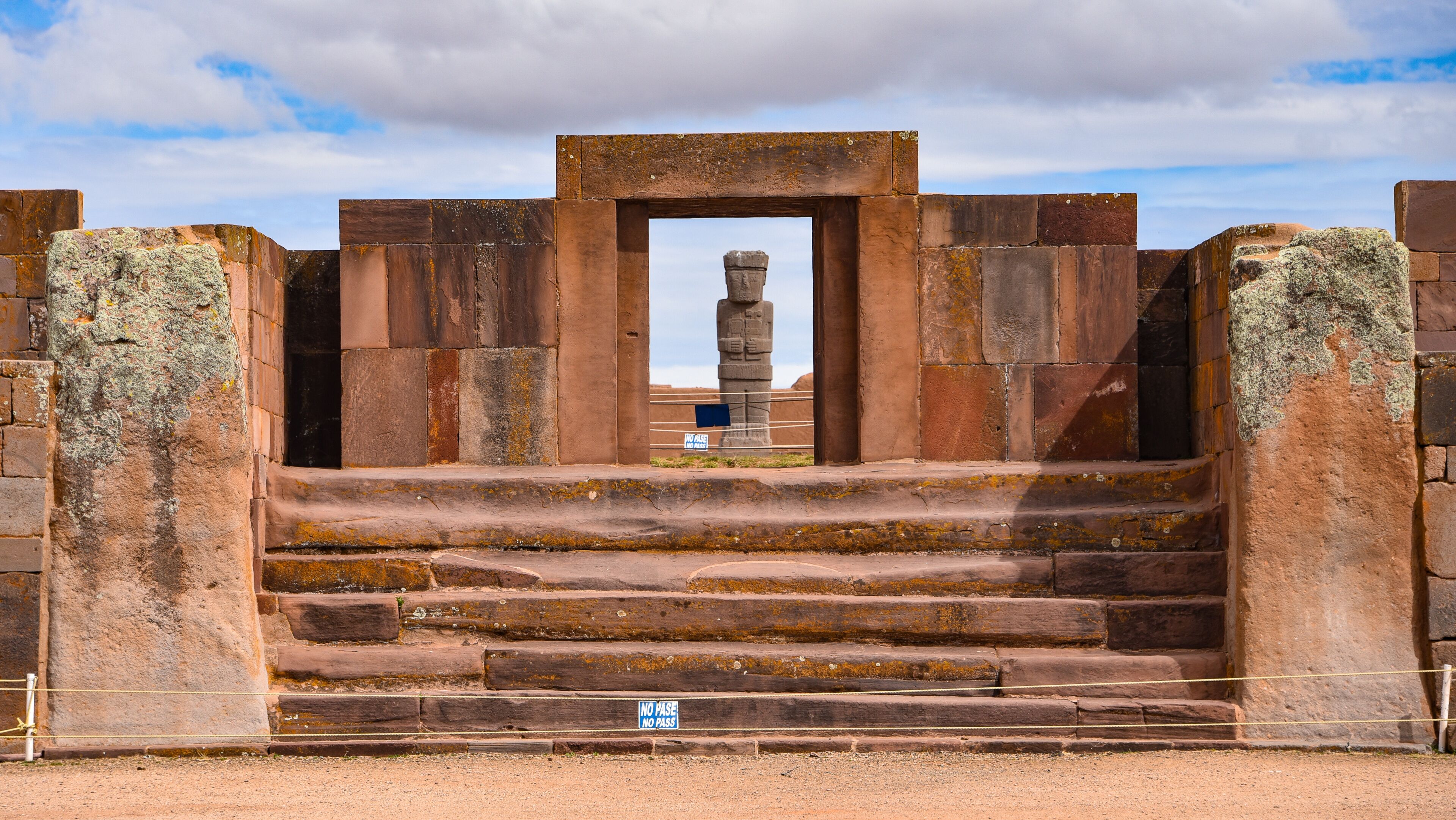 A stone staircase leading to a large stone structure with a central pillar, surrounded by walls.