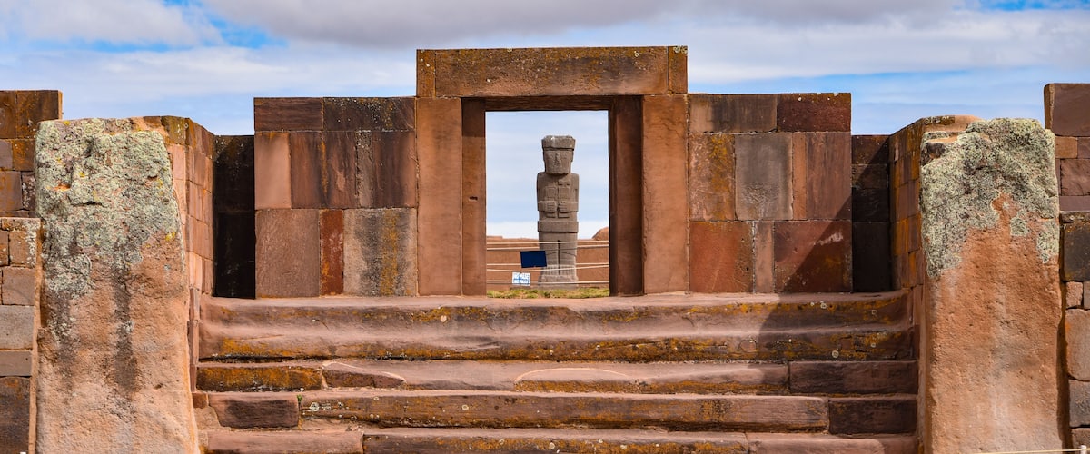 A stone staircase leading to a large stone structure with a central pillar, surrounded by walls.