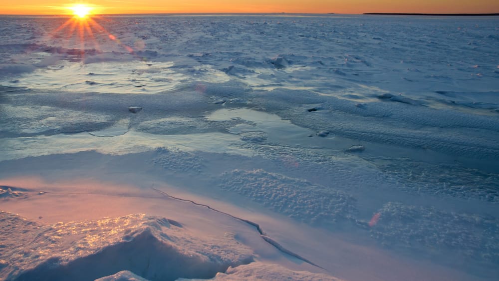 A frozen landscape with the sun setting over a flat, icy terrain.