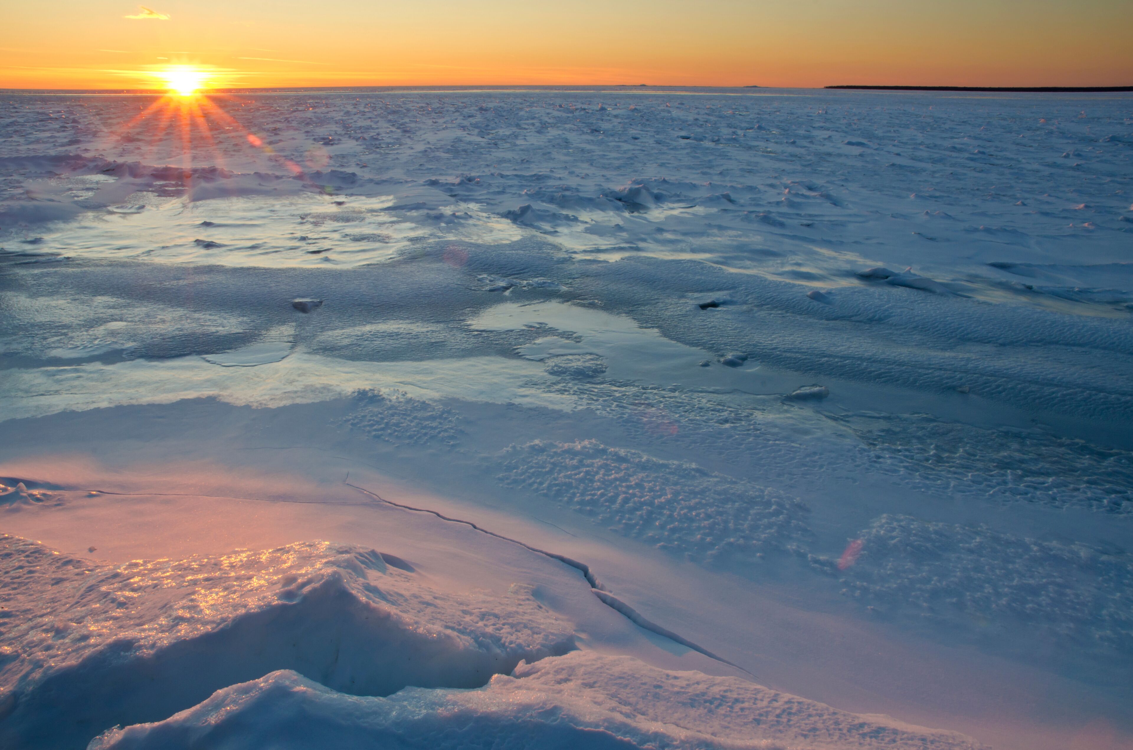 A frozen landscape with the sun setting over a flat, icy terrain.