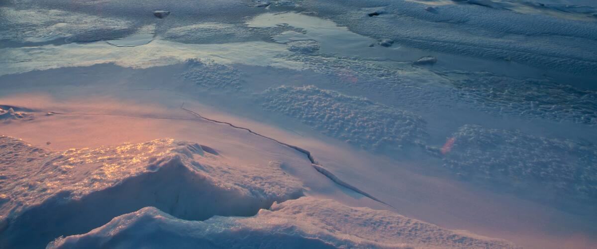 A frozen landscape with the sun setting over a flat, icy terrain.