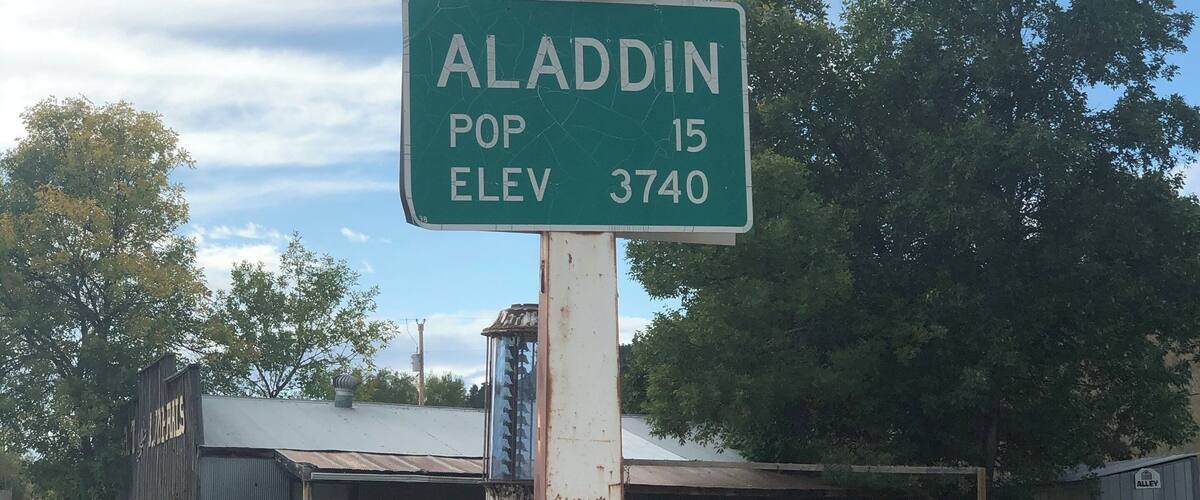 A gas station with a sign for Aladdin, a population of 15, and an elevation of 3740 feet.