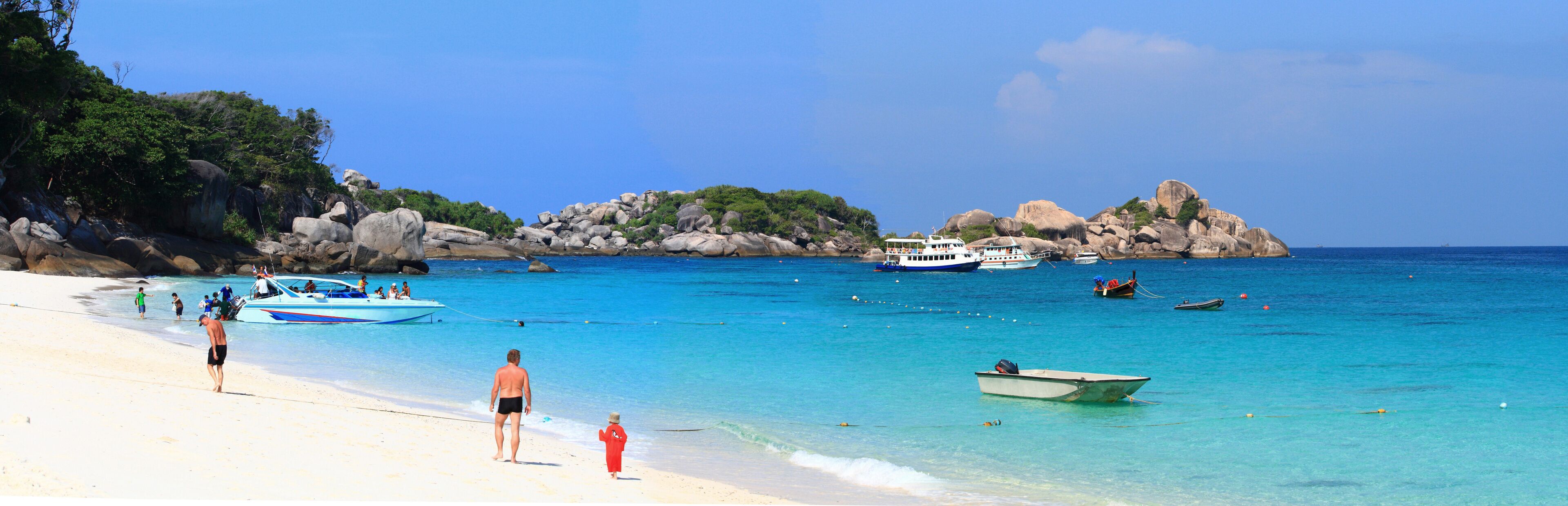 A beach with clear turquoise water, rocky outcrops, and several boats.