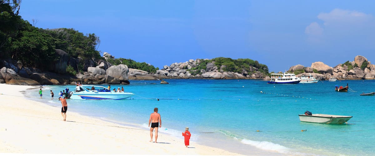 A beach with clear turquoise water, rocky outcrops, and several boats.