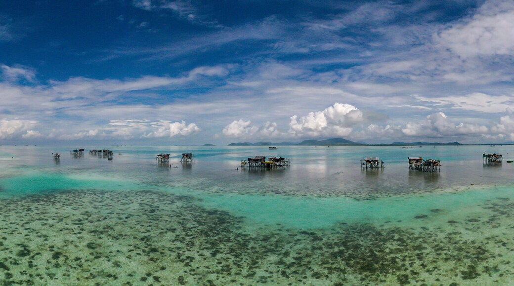 Aerial view of sea gypsy village over clear turquoise waters in Awan Biru Island Semporna, Sabah, Malaysia. Scenic seascape with coral reefs, coastal village, and blue tropical sky.