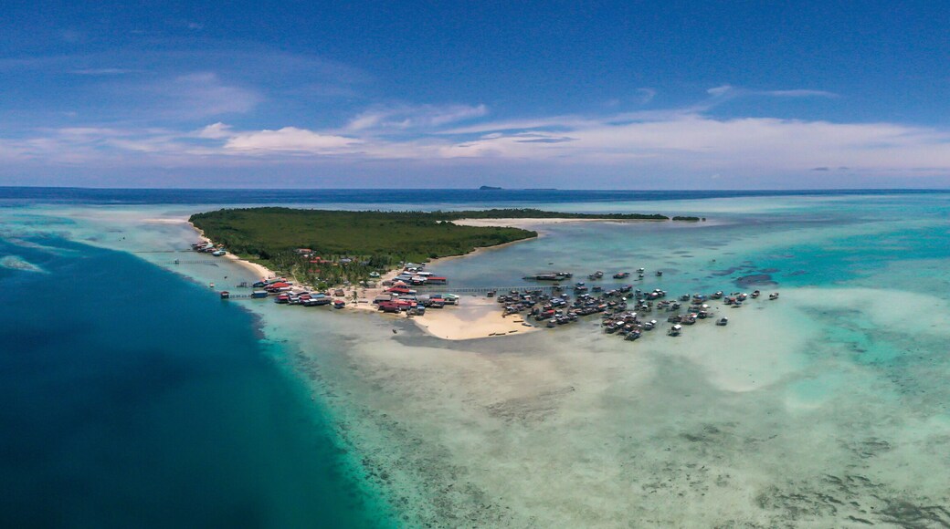 Aerial view of sea gypsy village over clear turquoise waters in Omadal Island Semporna, Sabah, Malaysia. Scenic seascape with coral reefs, coastal village, and blue tropical sky.