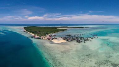 Aerial view of sea gypsy village over clear turquoise waters in Omadal Island Semporna, Sabah, Malaysia. Scenic seascape with coral reefs, coastal village, and blue tropical sky.