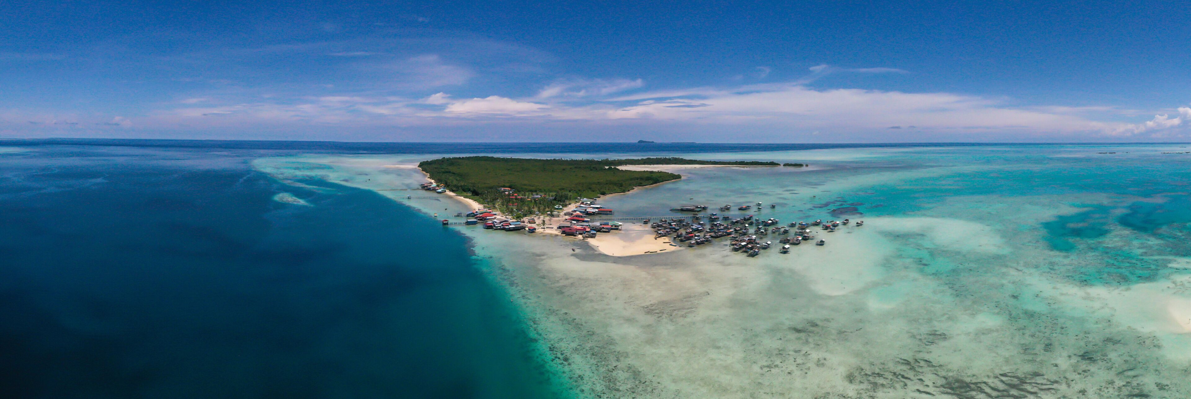 An aerial view of a tropical island with clear turquoise waters, a sandy beach, and a small dock with boats.