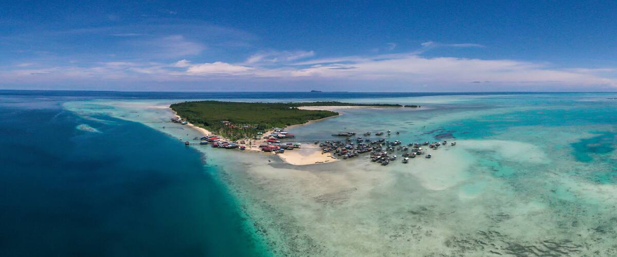 An aerial view of a tropical island with clear turquoise waters, a sandy beach, and a small dock with boats.