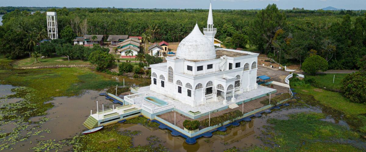 A white temple with a pointed roof and a spire, surrounded by water and greenery.