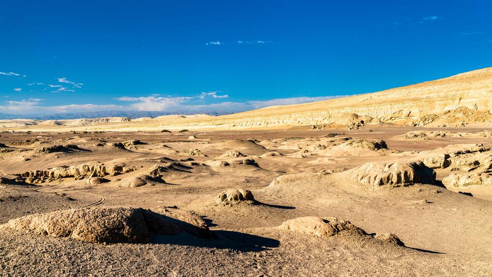 A vast desert landscape with rocky formations and distant mountains under a clear blue sky.