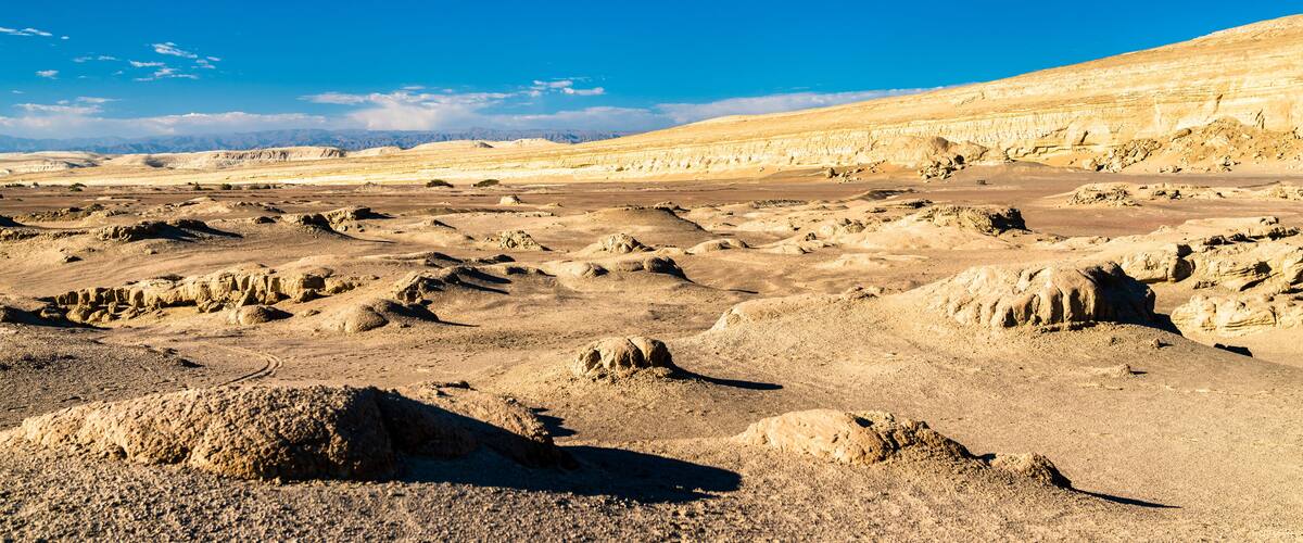A vast desert landscape with rocky formations and distant mountains under a clear blue sky.
