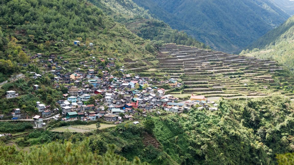 A terraced village nestled in a mountainous valley with dense greenery and traditional houses.