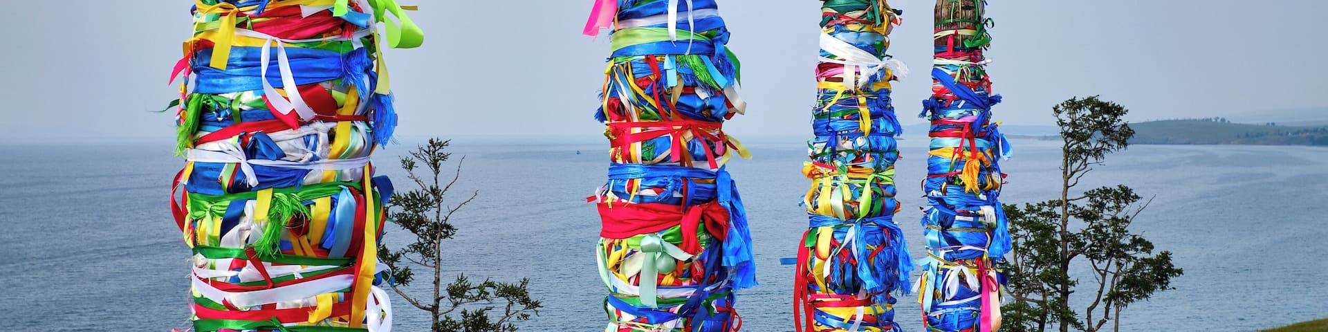 #Adventure Contest
Sacred shaman poles on Olkhon Island, called the heart of Lake Baikal.
The Shaman Rock is one of the nine most holy places in Asia. 13 totem poles stand tall at the entrance, guarding the sacred rock, representing the 13 deities of Olkhon and bearing colorful ribbons, known as ‘Khadag’, placed by pilgrims. The five colors symbolize different aspects of the environment. Blue for the eternal sky, green for the earth, yellow for religion, red for fire, white for milk.