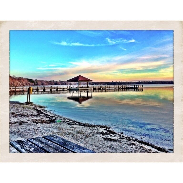 A wooden pier extending into a calm body of water with a gazebo at the end.