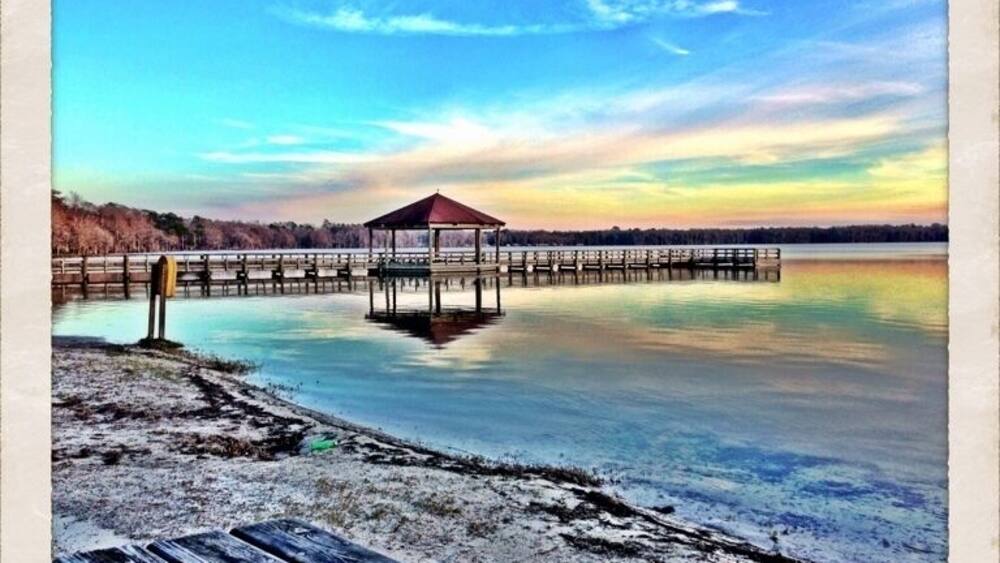 A wooden pier extending into a calm body of water with a gazebo at the end.