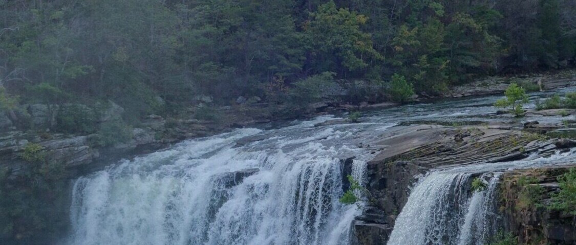 Una cascada que se precipita sobre un risco rodeado de un bosque denso.