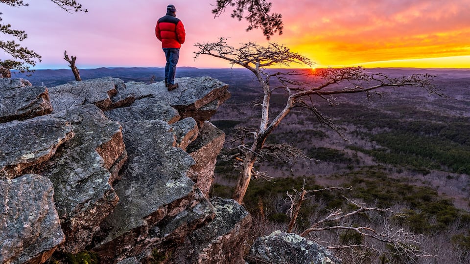 A person standing on rocky terrain overlooking a vast landscape during sunset.