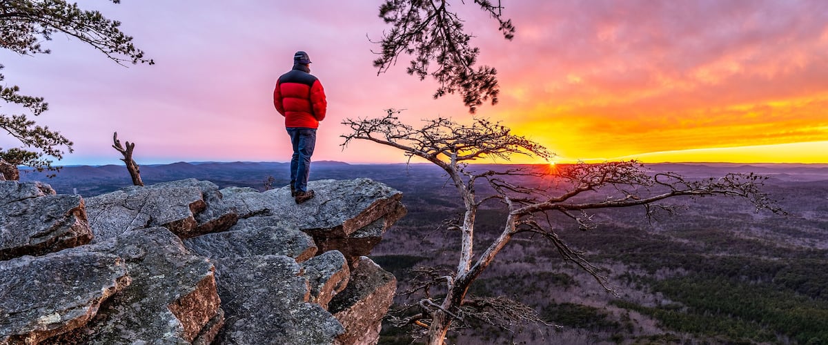 A person standing on rocky terrain overlooking a vast landscape during sunset.