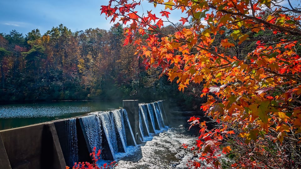 A waterfall cascading over a dam with autumn foliage in the foreground.