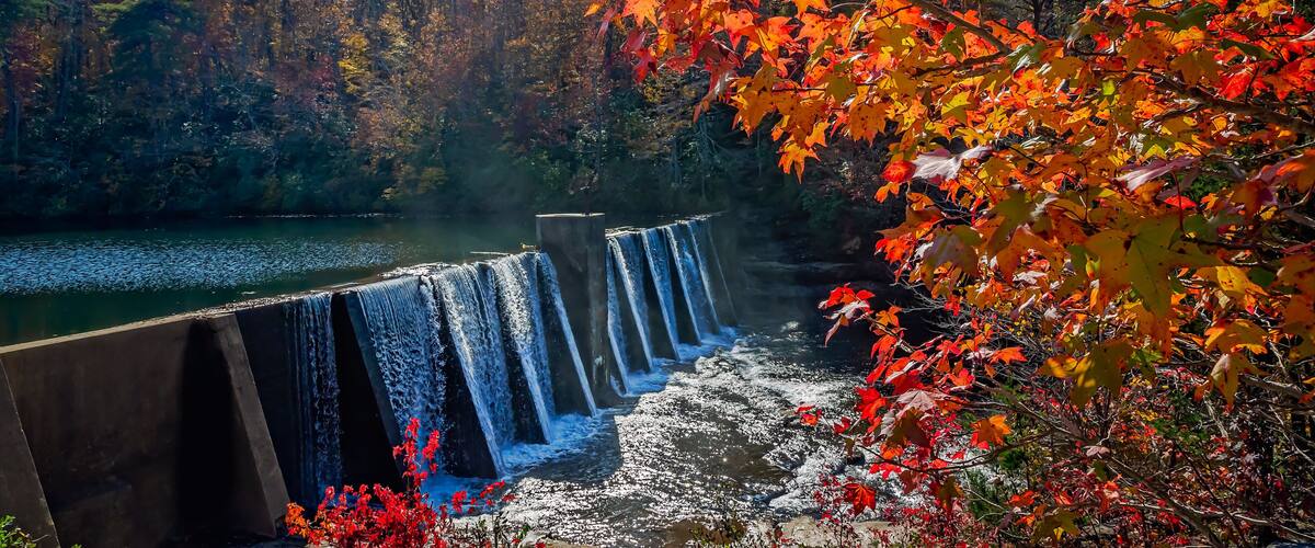 A waterfall cascading over a dam with autumn foliage in the foreground.