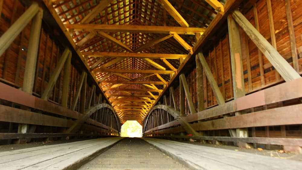 A wooden covered bridge with a central walkway and a lattice roof structure.