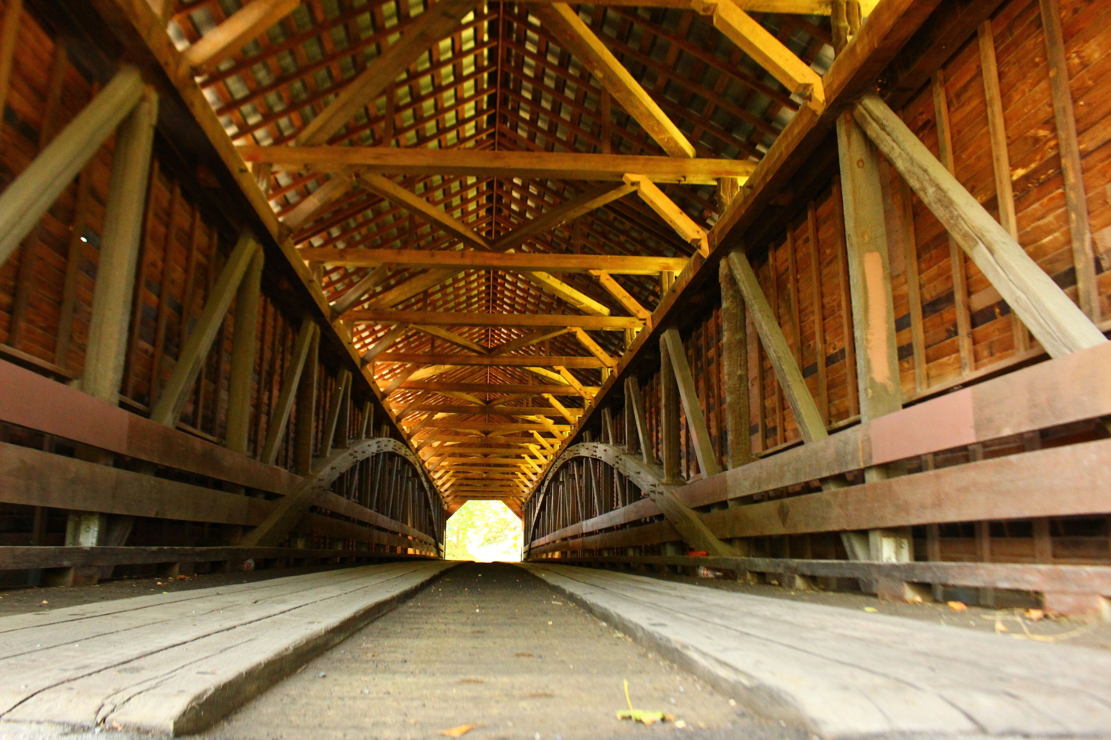 A wooden covered bridge with a central walkway and a lattice roof structure.