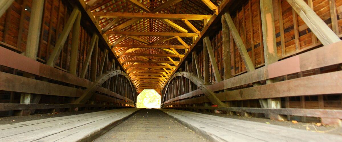 A wooden covered bridge with a central walkway and a lattice roof structure.