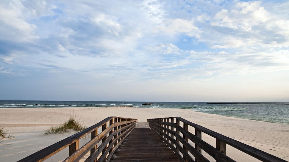 A wooden boardwalk leading to a sandy beach with the ocean in the background.