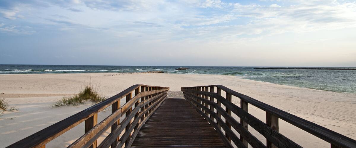A wooden boardwalk leading to a sandy beach with the ocean in the background.