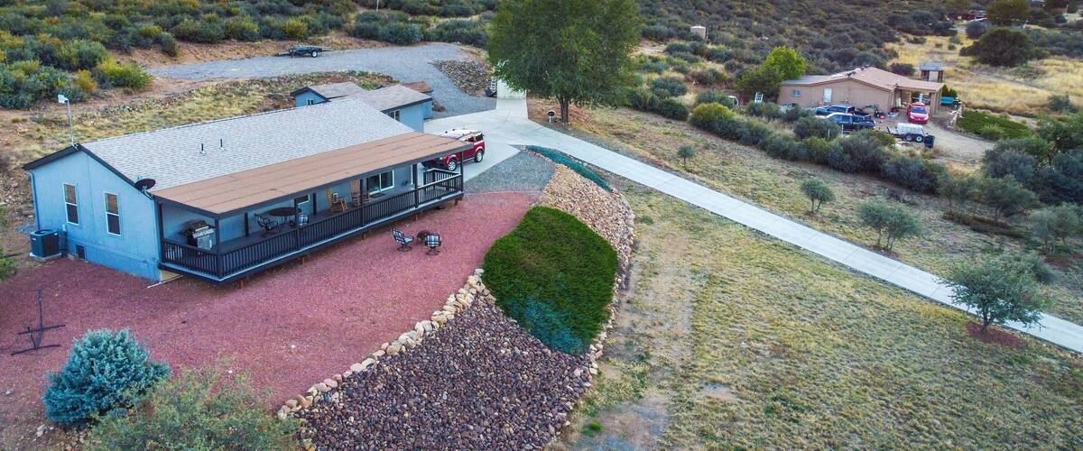 A residential area with a house featuring a covered patio, a gravel driveway, and a red-tiled roof.