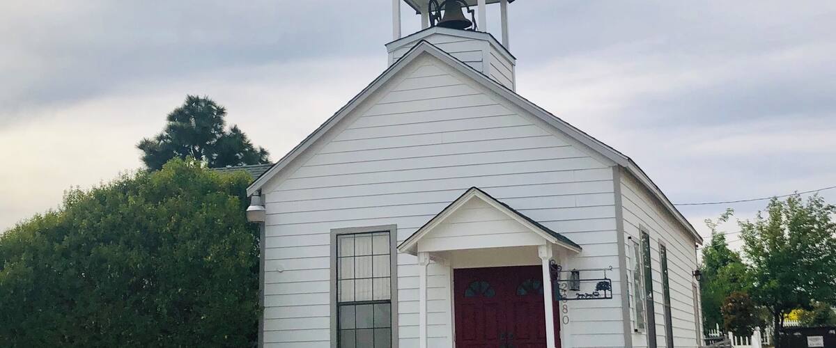 A white church with a red door, a bell tower, and a cross on top.