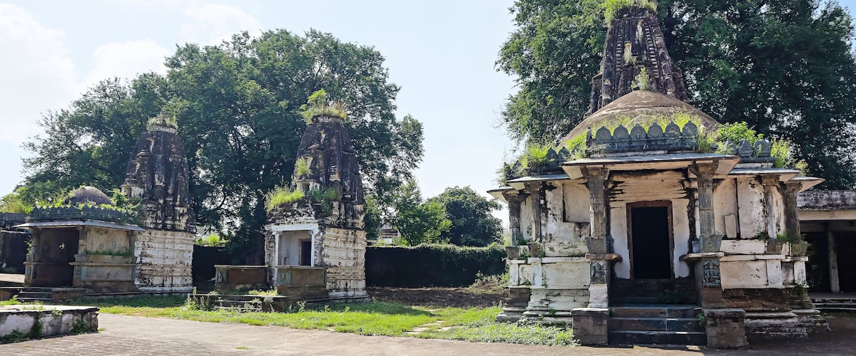Ancient stone structures with intricate carvings, surrounded by lush greenery and trees.