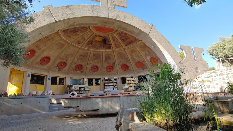 A large, arched building with a dome ceiling, a yellow door, and a small pond in the foreground.