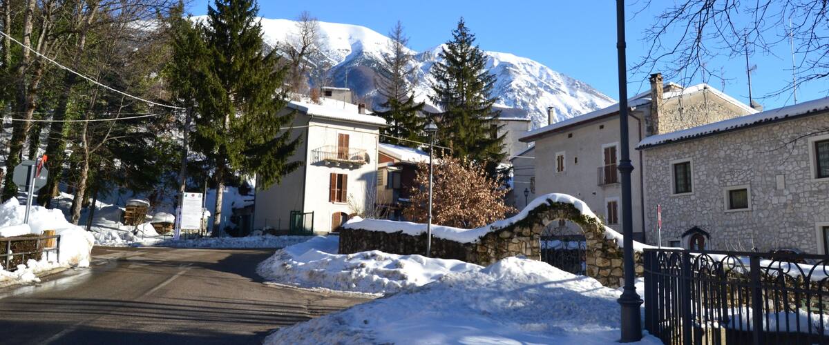 A snow-covered street with houses, a mountain in the background, and a lamppost.
